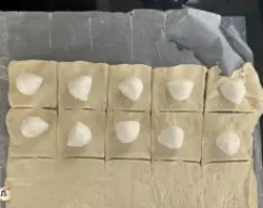 Step <p>Cortamos a masa, primeiro en tiras e despois en cubos duns 4 × 4 cm. Colocamos unha bola de queixo mozzarella no centro de cada cadrado de pasta (previamente escorrido da auga de almacenamento e secámolo con papel absorbente)</p> illustration